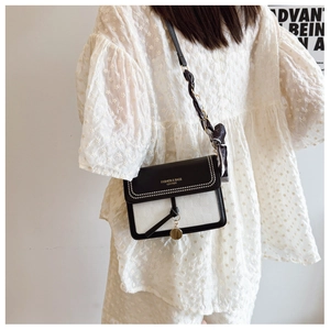 Detail of contrast cream square bag with pearl trim, silk scarf chain, and gold charm