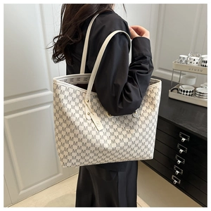 Detailed view of cream tote bag with repetitive M pattern and matching round charm hanging