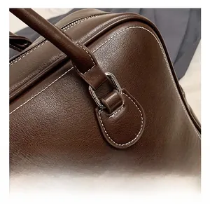Detail of dark brown leather tote featuring contrast white stitching and silver hardware