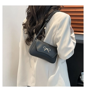 Détail du sac à bandoulière noir élégant avec un nœud décoratif en métal doré sur le rabat