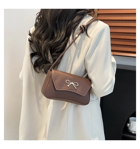 Détail du sac baguette en cuir marron foncé avec boucle nœud doré et bandoulière nouée