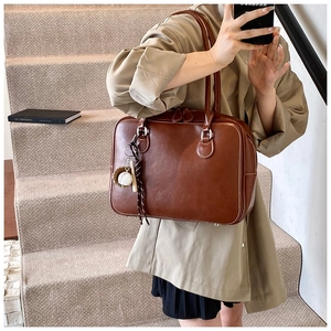 Detail of vintage brown leather tote bag with white contrast stitching and baseball charm
