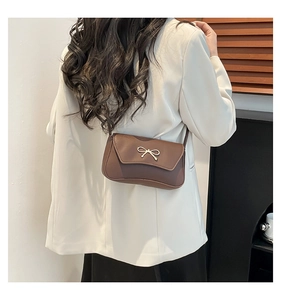 Détail d'un sac baguette marron vintage avec nœud doré sur une veste de costume