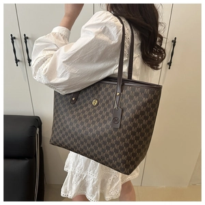 Detail view of large brown tote bag with M-pattern print and metallic logo on the side