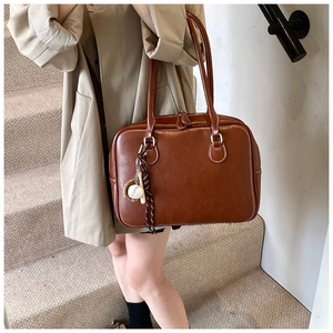 Close-up of vintage brown leather tote bag with white stitching and baseball charm