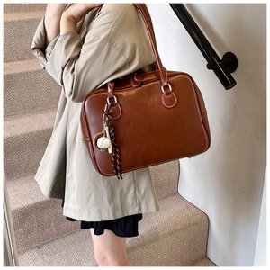 Macro detail of brown leather tote bag showing fine stitching and baseball charm
