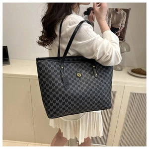Detail of a large black tote bag featuring repeating M prints and a gold circular M logo