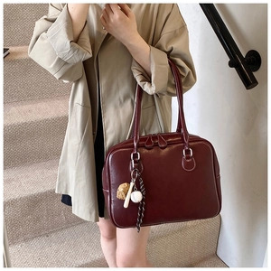 Detail showing high-shine burgundy leather shoulder bag with a unique baseball charm