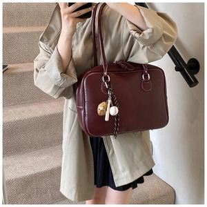 Deep wine red tote bag with baseball charm detail shown in a casual lifestyle setting
