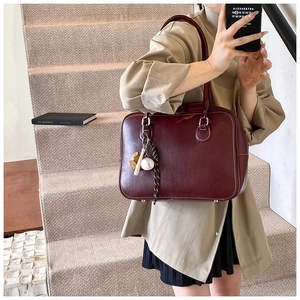 Detail of burgundy faux leather tote bag with contrast stitching and baseball charm