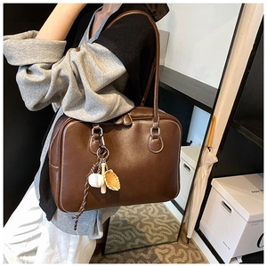 Detail of dark brown leather tote bag with white stitching and baseball charm