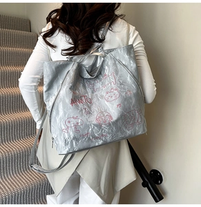 Detail of silver metallic tote bag featuring pink cartoon illustrations and AMITO logo