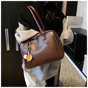 Detail of a brown leather shoulder bag with white stitching and sports charm accessory