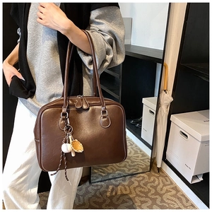 Detailed close-up of brown leather tote bag featuring a creative baseball glove charm