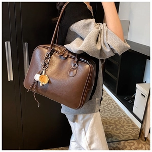 Side view of dark brown faux leather tote bag with baseball pendant in an indoor setting