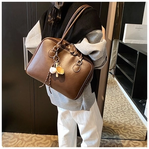 Brown leather Boston tote bag with unique baseball charms shown in a lifestyle setting
