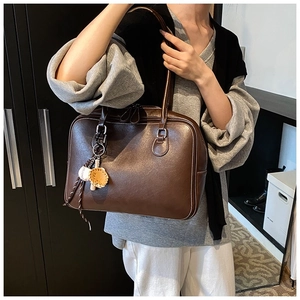 Detail view of brown faux leather tote bag with white contrast stitching and baseball charm