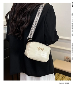 Detailansicht der cremefarbenen Tasche mit goldener Schleife und gemustertem Gurt