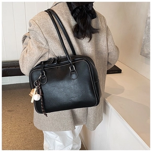 Close-up of black PU leather shoulder bag with white stitching and baseball charm