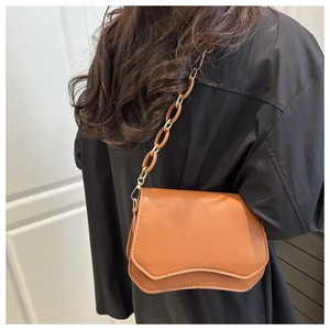 Side view of a brown textured crossbody bag with wavy flap design on a black outfit