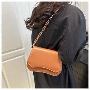Detail of caramel crossbody bag with wavy bottom and resin chain strap on shoulder