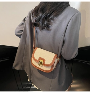 Close-up of contrast canvas saddle bag with brown leather trim and golden lock detail