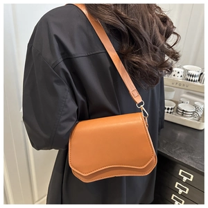 Caramel brown leather crossbody bag with wave flap design and gold chain strap in use