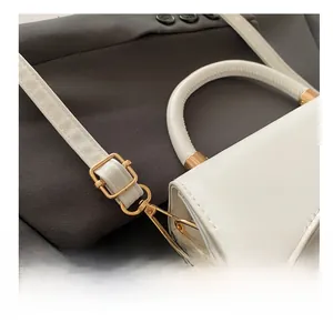 Detail view of adjustable gold metal hardware on a white leather minimalist crossbody bag