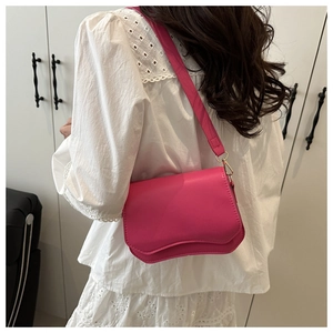 Detail view of a rose red shoulder bag with wave cut flap on a white lace top