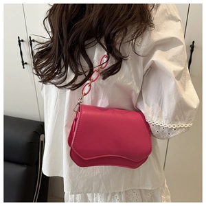 Detail of rose pink shoulder bag featuring wavy flap design and acrylic chain strap