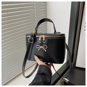 Detail of black box bag featuring gold bow accent, leather handle, and zipper
