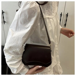 Detail of a dark brown glossy leather crossbody bag with a unique wavy flap and gold buckle