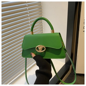Detail view of bright green trapezoid handbag with gold oval twist lock and smooth leather texture