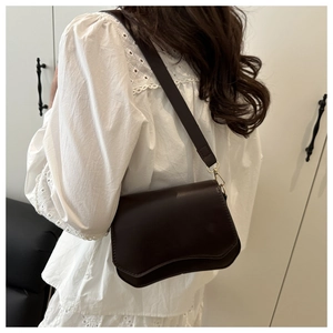 Detail of a dark brown crossbody bag with scalloped flap and wide strap on a model