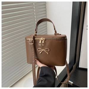 Detail of a brown leather box bag featuring a gold bow accent and dual zippers