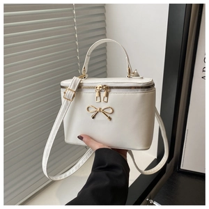 White box handbag with gold bow detail and adjustable strap shown in hand