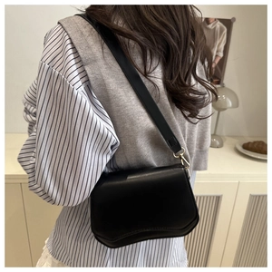 Detail of black crossbody bag with wave-shaped bottom and gold metal hooks worn on shoulder