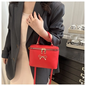 Detail of red French box bag with gold bow and adjustable shoulder strap on model