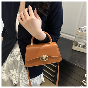 Close-up of caramel brown handbag with golden oval metal lock and smooth leather texture