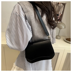 Side view of black leather crossbody bag with curved flap and golden metal buckle details