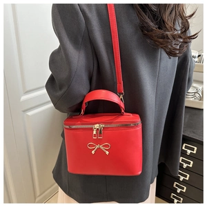 Macro detail of red leather box bag featuring a decorative gold bow and crossbody strap