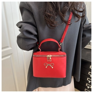 Detail of red box handbag with gold bow hardware worn with a grey blazer outfit
