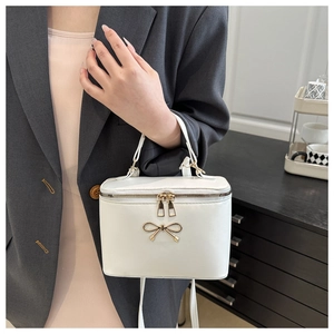 Close-up of stylish white box bag with gold bow ornament and dual zipper closure