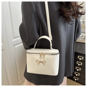 Detail of white PU leather box bag featuring a decorative golden bow and gold zipper