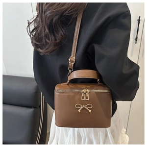 Detailed view of a brown box-shaped handbag with golden bow detail and top handle