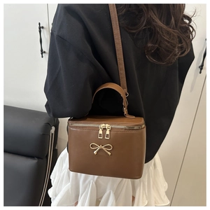Detailed back view of a dark brown box bag with golden bow and thin shoulder strap