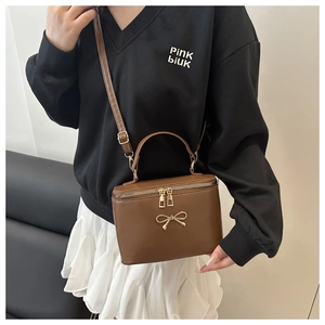 Detail of a brown leather box bag featuring a gold bow buckle and dual zippers