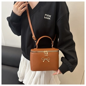 Detail of caramel brown box bag with gold bow hardware and top double zipper closure