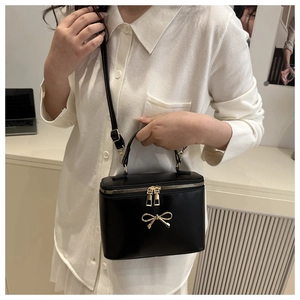 Detail of black box bag with golden bow buckle and dual zipper carried by a model