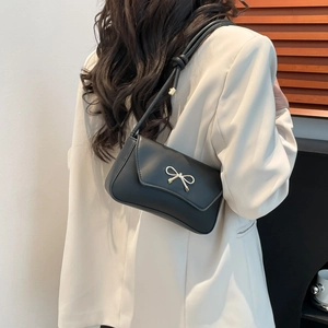 Sac sous le bras noir élégant avec boucle nœud doré porté sur un blazer de couleur crème